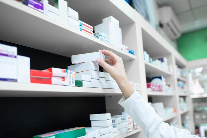 Closeup view of pharmacist hand taking medicine box from the shelf in drug store.